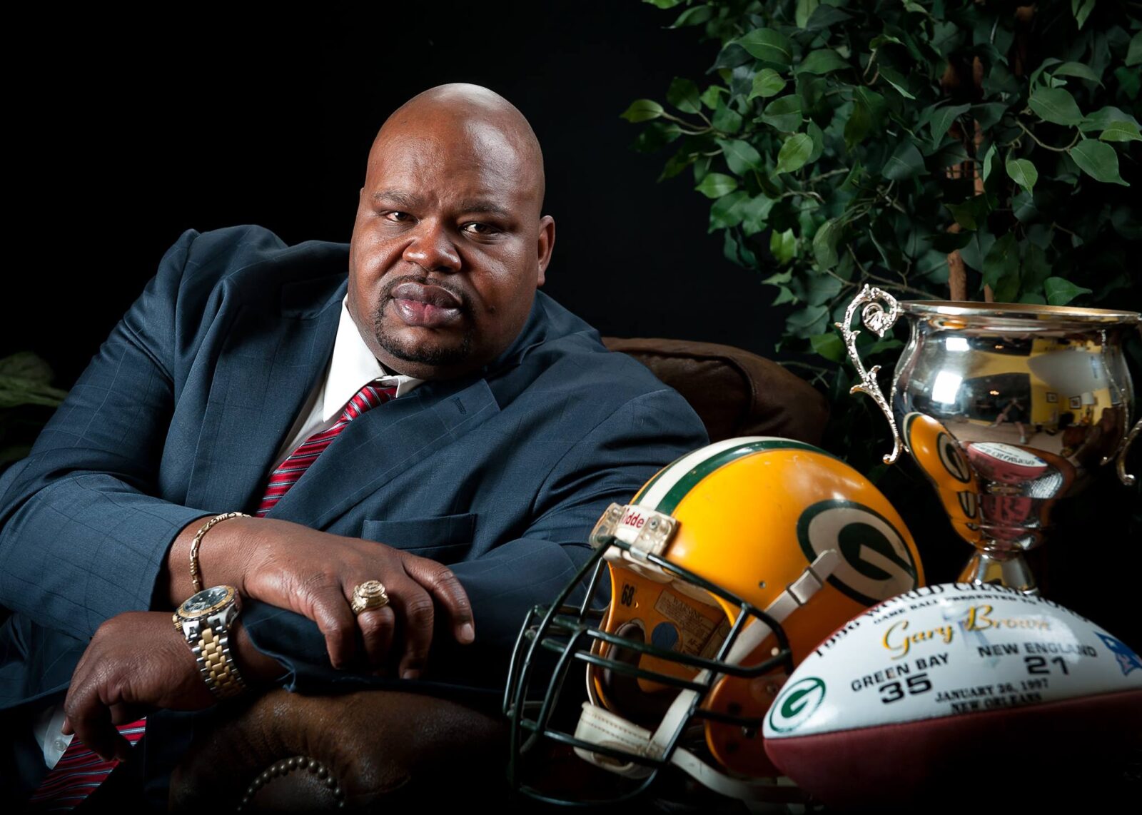 Man in suit sitting beside a football helmet and signed ball.