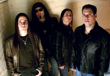 Four men with long hair and dark clothing pose against a wall.