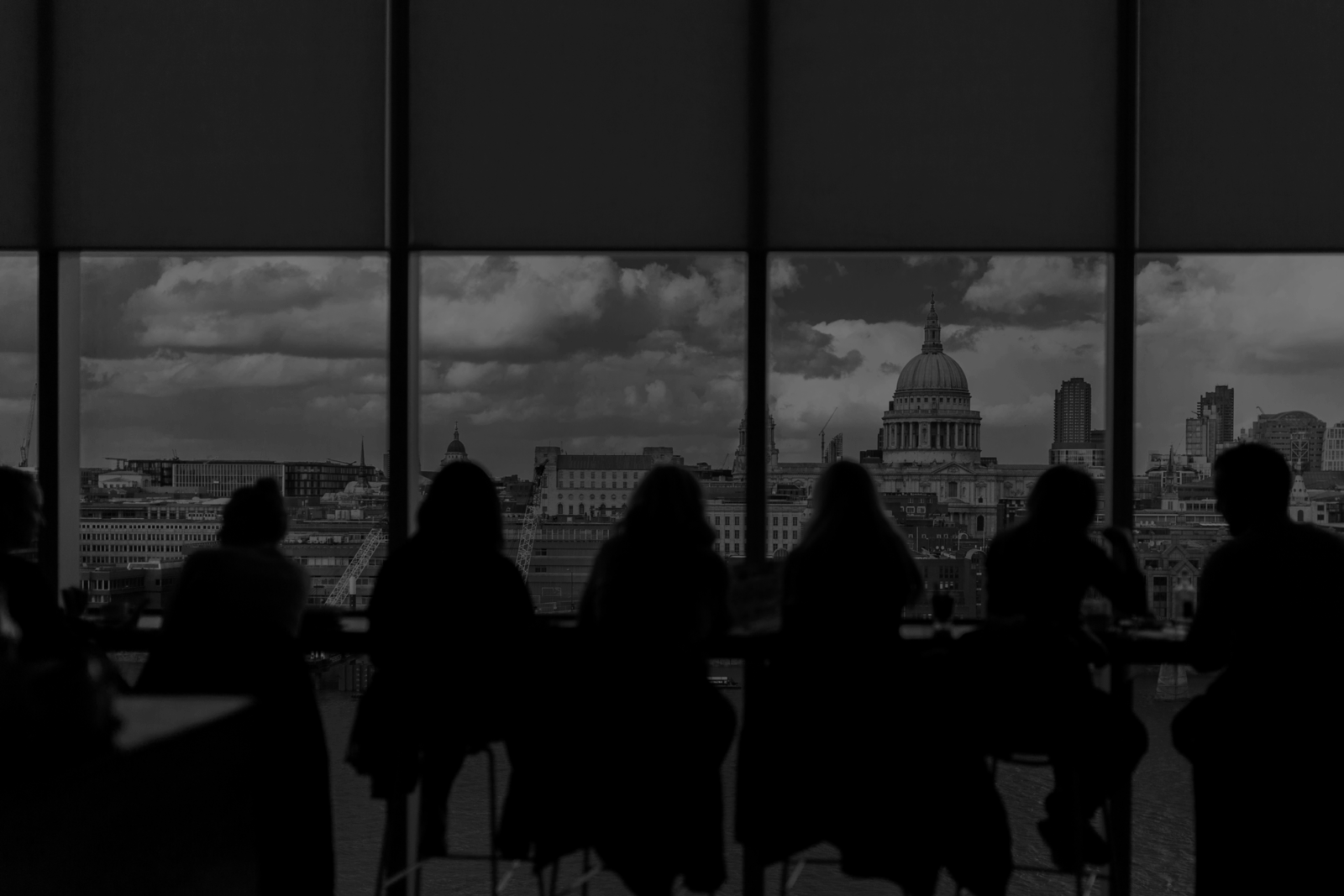 Silhouettes of people seated by a large window with a cityscape view.