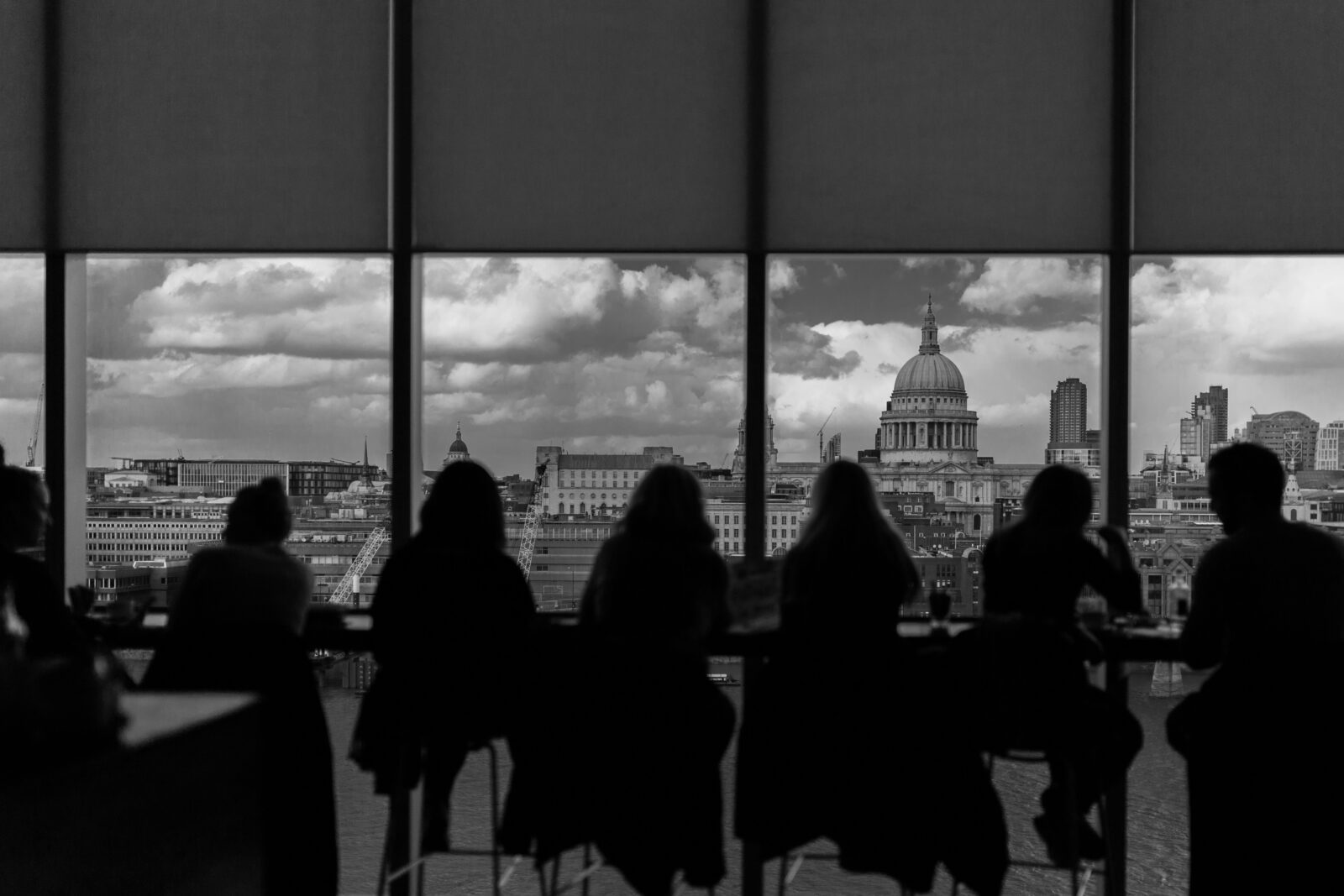 Silhouettes of people seated by a large window overlooking a cityscape with a dome structure.