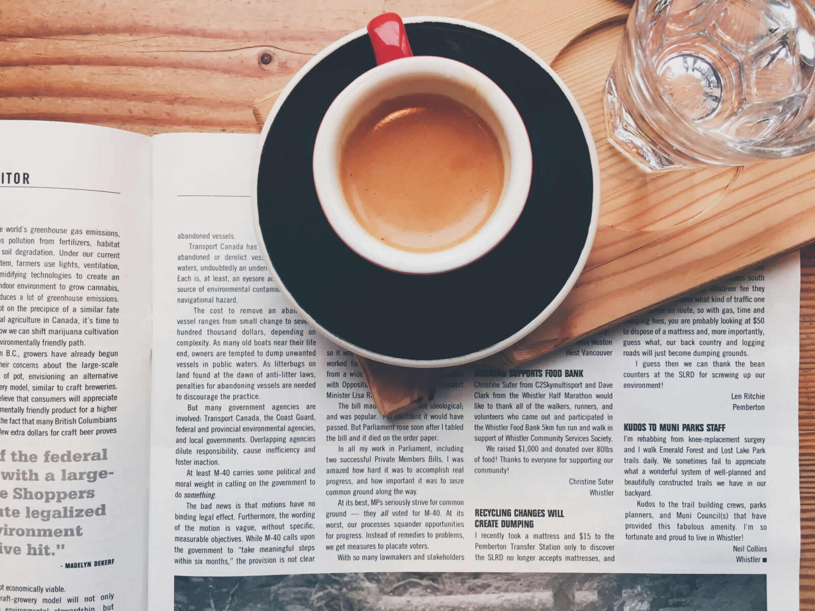 A cup of coffee on a black saucer atop an open book and newspaper.