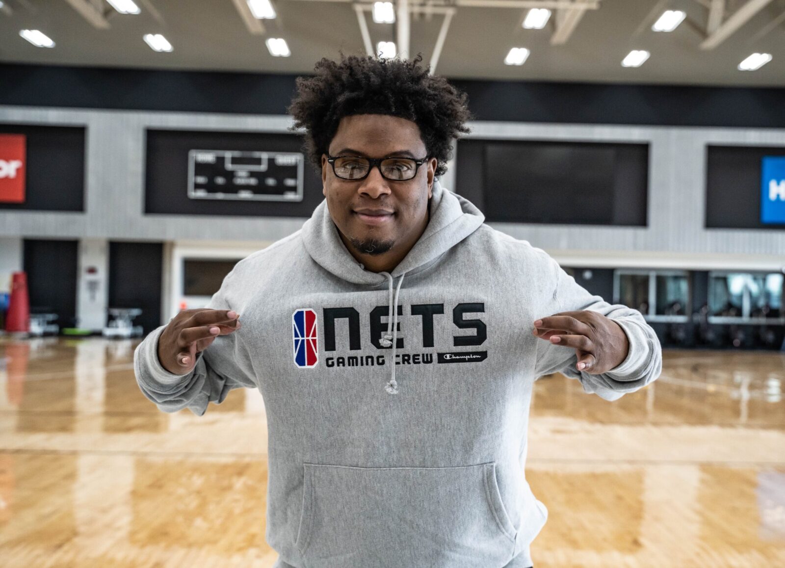 Man in a gray Nets hoodie posing indoors with peace signs.